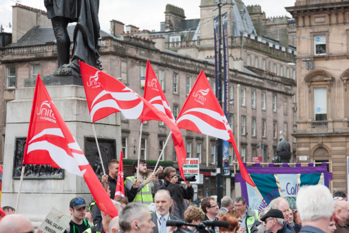 Glasgow, UK - June 30, 2011: Members of the Unite trades union hold red and white union flags at a demonstration against cuts to pay and pensions held in Glasgow's  George Square. They are standing on the steps of the statue of Robert Burns.