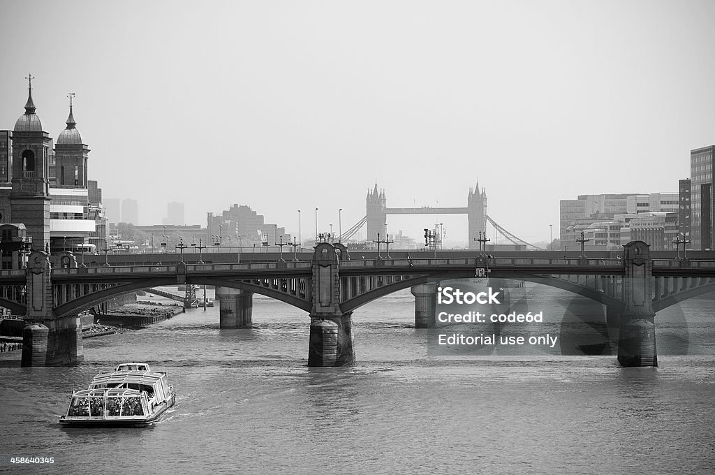Thames River with tourist boat, City of London London, United Kingdom - April 24, 2011: Thames River with Southwark Bridge and Tower BRidge in the background. A tourist boat on the left. Black-and-white photograph with copy space. The Thames River runs through Greater London and was used for transporting goods to the City of London. Tower Bridge is a famous London landmark, one of the few suspension bridges, it leads traffic over the Thames River, connecting the City with Southwark. Black And White Stock Photo