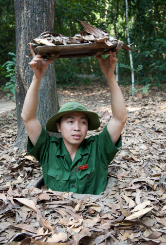 Ho Chi Minh City, Vietnam - January 20, 2009: The Cu Chi tunnels were used by the Viet Cong guerrilla during the Vietnam war. The tunnels are located 35 km from  Ho Chi Minh City. A guide shows the entrance to the tunnels. The tunnel hatch is covered with leaves and is very hard to see. The guide is dressed in a viet cong uniform. The pin in the hat has the symbol of Viet Cong.