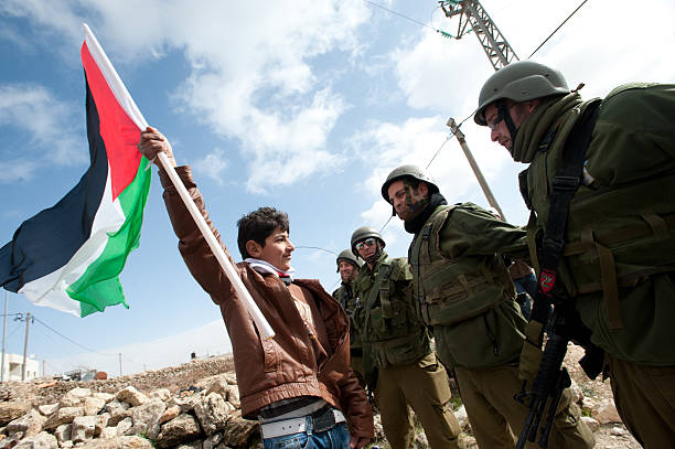 West Bank Anti-Wall Demonstration "Al-Masara, Occupied Palestinian Territories - January 27, 2012: A Palestinian youth waves a flag while confronting Israeli soldiers in a protest against the Israeli separation barrier in the West Bank down of Al-Masara." historical palestine photos stock pictures, royalty-free photos & images