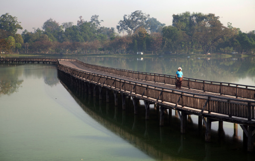 Yangon, Myanmar - February 16, 2011: A Burmese woman walking along a bridge on Kandawgyi lake, also known as the Great royal lake. The Kandawgyi lake was artifically created to provide a clean source of water supply for the city during the British colonial administration. Water from Inya lake is channelled through a series of pipes to fill the lake.