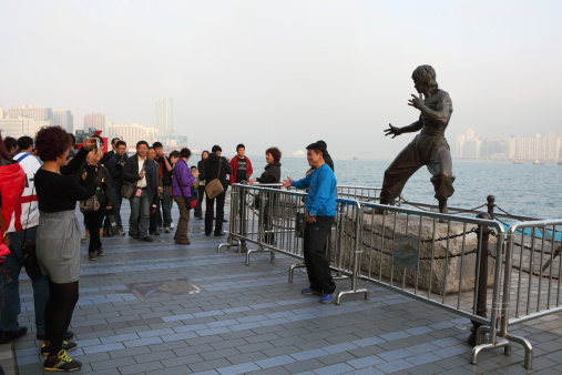 Hong Kong, China - February, 25th 2011: Many mainland tourists taking photo in front of Bruce Lee\'s statue along the Avenue of Stars in Tsim Sha Tsui, Hong Kong. Avenue of Stars is a new tourist attraction and features plaques and hand prints of movie stars in Hong Kong.