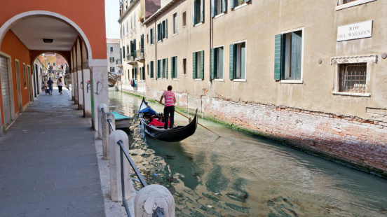 Venice, Italy - May 23, 2011: Gondolier in Rio del Magazen, one of Venice canals. Some tourists on the canal side, under a porch and crossing a bridge