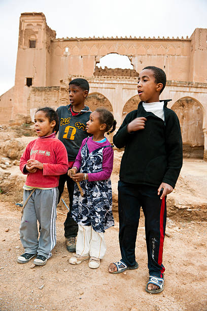Taliouine, Morocco - March 28th, 2012:Four curious children, two boys and two girls, standing in front of Kasbah ruins in Taliouine and watching tourists.