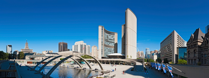 Toronto, Canada - September 9th, 2011: Clear blue summer skies above the landmark twin towers of City Hall overlooking locals and tourists passing through the urban plaza of Nathan Phillips Square with its three Freedom Arches and reflecting pool. Composite panoramic image created from nine contemporaneous sequential photographs.