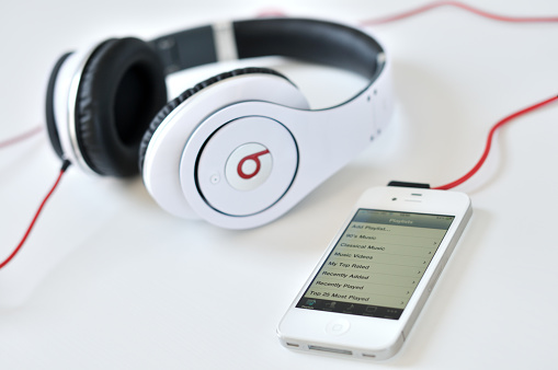 Budapest, Hungary - September 3, 2011: White Beats by Dr. Dre Studio over ear headphones by Monster and a white iPhone version 4 (shows playlist) on a white table.