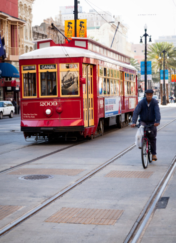 New Orleans, Louisiana, United States- March 31, 2011: Black man cycling next to the typical street car of New Orleans along Canal street, main road of the city.