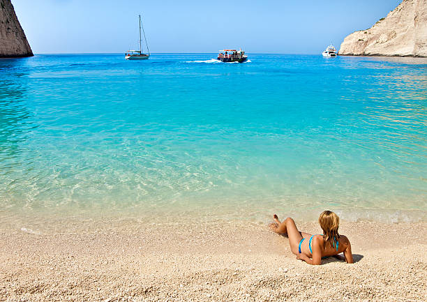 Zakynthos island, Greece - September 2nd, 2008: A girl is sunbathing at Navagio beach. Two boats are anchored and one is cruising in the background.