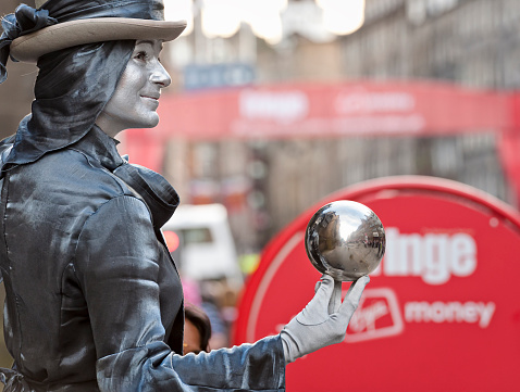 Edinburgh, Scotland - 5th August 2011: On the opening day of the Edinburgh Festival Fringe, a street performer with a silver painted face holds a polished metal sphere to show a reflected image of the Royal Mile.