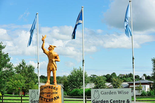 Dumfries, Scotland - August 14, 2011: A wooden statue of Peter Pan on the roadside at the entrance to Garden Wise garden centre. The statue was carved by local wood carver Rodney Holland and unveiled by actress Joanna Lumley. Peter Pan author JM Barrie spent time as a child at Moat Brae House in Dumfries, and later said it was \