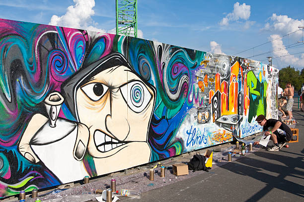 Detail of a Graffiti Action Potsdam, Germany - August 8, 2011: Detail of a Graffiti Action. A young man is painting with a spray can a colorful graffiti on the wall. Young people have got the chance to design with her own graffiti a long construction hoarding around a construction site during a street art event in Potsdam. bunt stock pictures, royalty-free photos & images