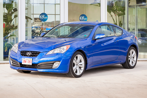 Saint John, New Brunswick, Canada - April 29, 2012: Hyundai Genesis Coupe on display at a car dealership and in front of the showroom.  Behind vehicle, advertisements and interior of showroom are pictured.  The Genesis Coupe is a sports car made by Hyundai.  It is a rear-drive platform and is available with multiple engine variants.
