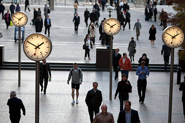Pedestrians walking past clocks in Canary Wharf London's Financial District stock photo