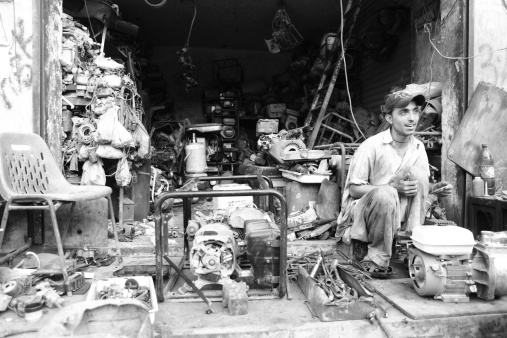 Karachi, Pakistan - June 17, 2010: An adult Pakistani worker at a power generator repair workshop in Shershah Kabari Market (scrapyard) in Karachi, Pakistan. Located in old city area of metropolis Shershah's junkyard is home of few hundreds shops dealing in scrap items ranging from auto parts to industrial junk imported from developed world to recycle in foundries or to give another lease of life through this market.