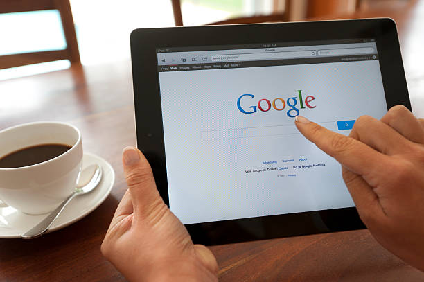 female hand holding an ipad showing google. - google stockfoto's en -beelden