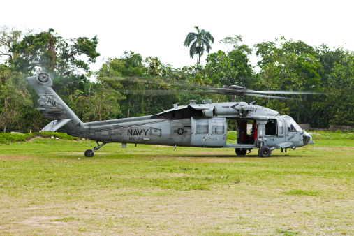 Milot, Haiti - January 29, 2010 : A US Navy Sikorsky SH-60 Seahawk ready for take off stands in an open field waiting for injured Haitians to be loaded on board. The U.S. Coast Guard and Navy helicopters have been transporting the most severely injured to the town of Milot where many temporary hospitals have been set up to help them. The Sikorsky SH-60/MH-60 Seahawk is a twin turboshaft engine, multi-mission US Navy helicopter, its most significant part being the airframe modification, which is a hinged tail to reduce its footprint aboard ships.The earthquake of 2010 with a magnitude of 7.0Mw caused massive destruction to property and life in Haiti.