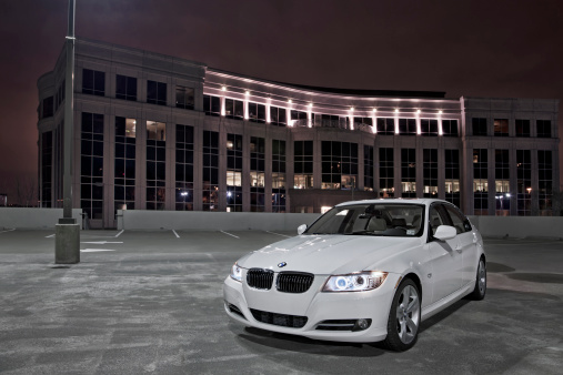Nashville, Tennessee, USA - March, 7th 2011: A white 2011 BMW 335i luxury sport sedan with glowing blue angel eye headlights, taken at night on top of an illuminated parking deck in front of a modem office building in Nashville TN.