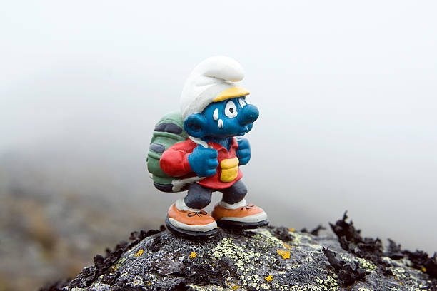Quito, Ecuador - September 21, 2008: Smurf puppet with backpack walking outdoors, on a rock with mist on background. Selective focus.