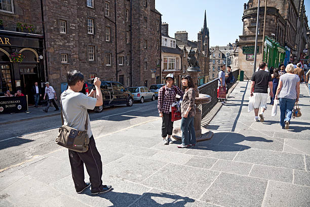 Edinburgh, Scotland, UK - 3rd July, 2011: Asian tourists having their photo taken beside the statue of Greyfriars Bobby while other people walk along George IV Bridge and Candlemaker Row, Edinburgh.Greyfriars Bobby was a Skye Terrier who famously guarded his deceased owner's grave until he himself died in 1872. Baroness Burdett-Coutts, a famous English philanthropist, donated the statue of the dog to the city in 1873.