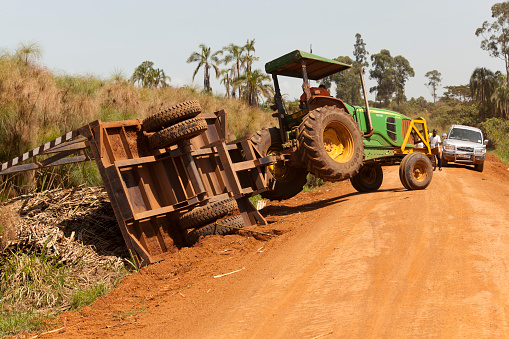 Masindi, Uganda - December 21, 2011: Overload Tractor trailer is overturned at Hoima - Masindi road at Uganda, at Africa. He is calling his chief for inform the accident and cars are waitng to the other side of the tractor.