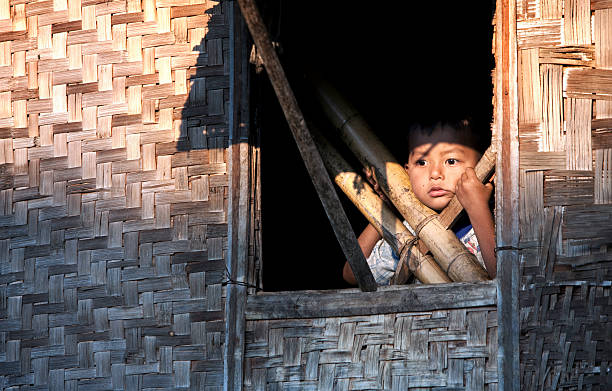 Inle Lake, Myanmar - March 2, 2011:A child looking out of the window of his home in one of the floating villages built on stilts on Inle lake. Around 70000 people live on Inle lake in numerous floating villages built along the shallow parts of the lake. The houses are built on stilts and are made of wood and woven bamboo. The villagers are largely self sufficient farmers using floating gardens to grow what they can.