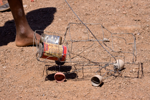 Khorixas, Namibia - April 9, 2009: A young boy at the Jacob Basson Combined School grounds in Damarland near the town of Khorixas in Namibia plays with homemade wire, bottle cap and tin can vehicle toy.