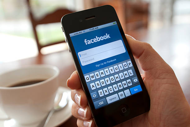 Sydney, Australia - October 28, 2011: Female hand holding an iphone showing the Facebook login page. There is coffee on the dining table in the background.  This image shows the iphone being used in a casual environment.