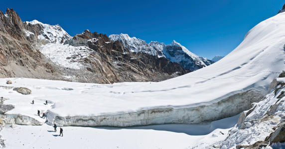 Solu Khumbu, Nepal - October 27th, 2011: Mountaineers and Sherpas crossing the icy bergschrund onto a snowy glacier on the high altitude Cho La pass below Labuche deep in the Himalaya mountain wilderness of the Sagarmatha National Park. Composite panoramic image created from seven contemporaneous sequential photographs.