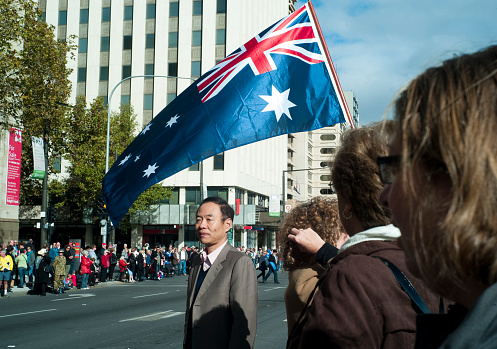 Adelaide, Australia - April 25th, 2012: Asian man walks underneath Australian Flag during the ANZAC day parade in Adelaide