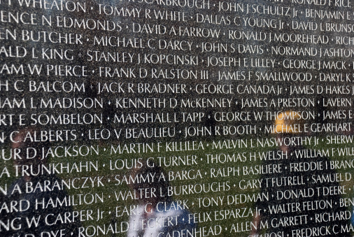 Washington DC, USA - April 10, 2008: One of the stone panels that make up the Vietnam Veterans Memorial, inscribed with names of the dead. Visitors to the memorial are reflected in the stone.