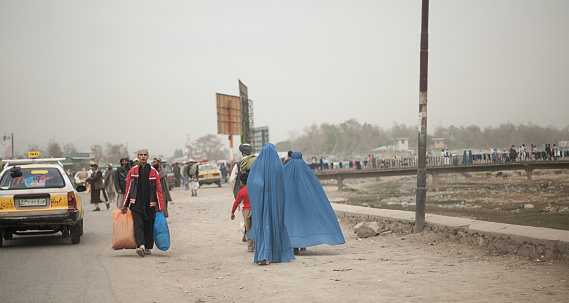 Kabul, Afghanistan - November 7, 2008: A man walking towards the the bazaar and two women walking towards the bridge that crosses Kabul River.