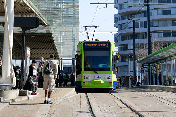 Croydon, England - March 25, 2012: A tram bound for Beckenham Junction in Kent, about to leave East Croydon tram station in Surrey. Both places are in the suburban Greater London area. The building on the right is affectionately known as The Threepenny Bit Building because of its unusual shape and is a relic of the 1970s. A number of people are waiting on the tram platforms or are entering the adjacent East Croydon railway station.