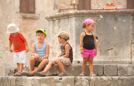 San Gimignano, Tuscany, Italy - August 29, 2011: Children sitting and talking at a fountain on the city square of San Gimignano in Tuscany.