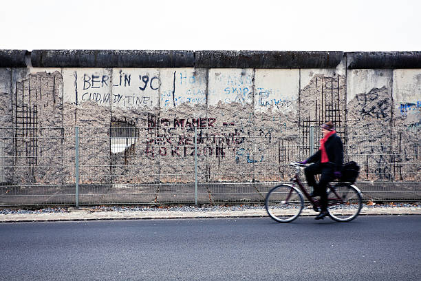 Man Cycling in Front of Berlin Wall, East Side, Germany Berlin, Germany - November 16, 2011: Man cycling along the last remains of the Berlin wall along the ex headquarters of the Gestapo and the SS in Niederkirchnerstrasse. east berlin photos stock pictures, royalty-free photos & images