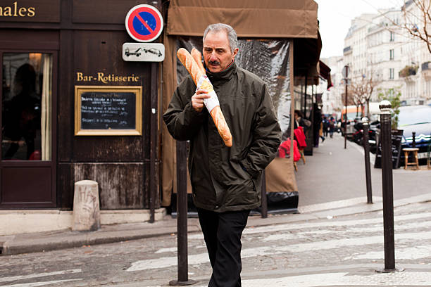 Paris, France - January 18, 2012: Man crossing the road with his baguette along the streets of Montmartre. The baguette is a typical french bread.