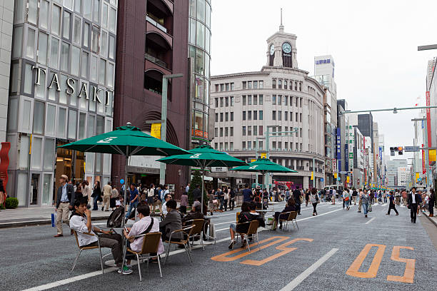 Tokyo, Japan - October 1, 2011 : People walking and sitting at Ginza in downtown Tokyo, Japan. Ginza shopping district, the most expensive real estate price in Japan. The historic building with a clock tower is the landmark in Ginza - The Wako store.