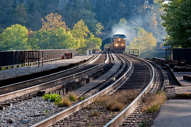 CSX Train Coming Through a Tunnel Harpers Ferry, WV, USA -- October 22, 2010: CSX Freight Train Engines Exiting a Mountain Tunnel Pulling a Large Number of Freight Cars.  CSX Transportation operates a Class I railroad known as the CSX Railroad in the United States, owned by the CSX Corporation. The company is headquartered in Jacksonville, Florida, and owns approximately 21,000 route miles. CSX operates one of the three Class I railroads serving most of the East Coast, the other two being the Norfolk Southern Railway and Canadian Pacific Railway. This railroad also serves the Canadian provinces of Ontario and Quebec. harpers ferry photos stock pictures, royalty-free photos & images