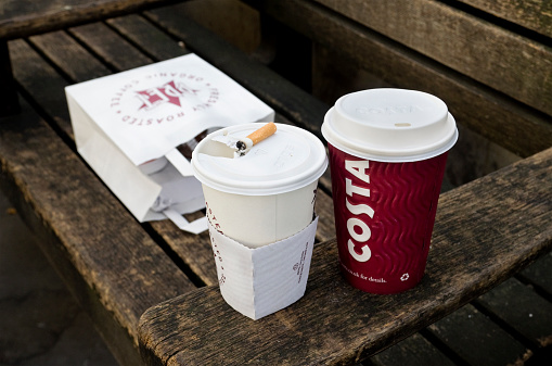 London, England - January 13, 2012: A group of litter items left by someone after their lunch break in St Paul's Churchyard, Central London, comprising two coffee containers, a carrier bag and a cigarette end. There was a waste bin next to the bench... (Taken on a dull winter day.)