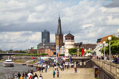 Düsseldorf, Germany - June, 18th 2011: View over promenade at riverside of river Rhine in Düsseldorf, North Rhine Westfalia. In background is historic center so called Altstadt. Tower in center of aperture is museum of navigation in old castle tower. Behind is church St. Lambertus. Area is all around square Burgplatz. Many visitors, tourists and people from Düsseldorf are walking around. On river a tourist boat is coming.