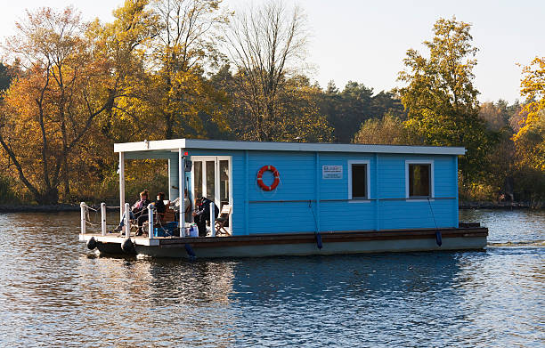 Blue Houseboat is crossing the River Havel Brandenburg, Germany - October 23, 2011: A beautiful blue houseboat is crossing the River Havel near the town Brandenburg. Tourists are sitting on the terrace of this wooden boat and enjoying the nature in the region Havelland. The sun is shining on this warm autumn day. In German the name of the ship is Bungalowboot, a connection of boat and holiday house. houseboat photos stock pictures, royalty-free photos & images