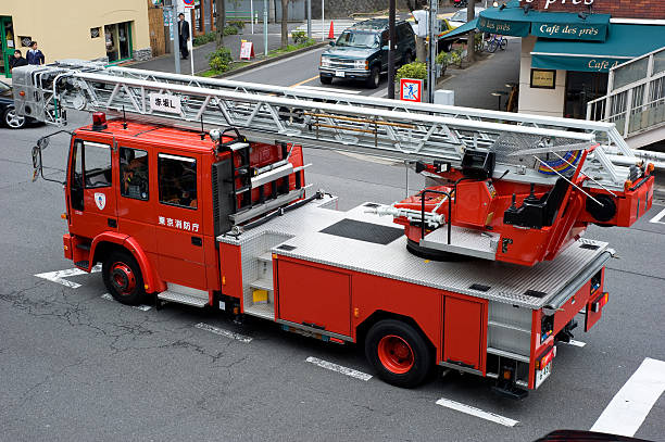 Tokyo, Japan - March 19th, 2010: A fire truck standing on the street in Hiroo, Tokyo, waiting for an opportunity to turn.  The street scene was taken during the middle of the day and also includes pedestrians walking along the footpath, as well as other vehicles standing at the crossing.  A cafe is also located at the corner of the crossing.
