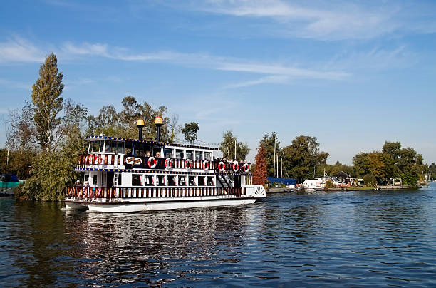 Horning, England - September 27, 2009: A tourist paddleboat on the River Bure at Horning, Norfolk, in the heart of the Norfolk Broads national park. The River Bure is the longest - and probably the busiest - of the rivers in Norfolk Broads: it winds between and connects many of the Broads - ancient peat diggings which filled with water and are now a hugely popular tourist destination, busy with pleasure craft and houseboats all through the summer months. The Bure runs from Coltishall to join the River Yare at Great Yarmouth and then to the North Sea.