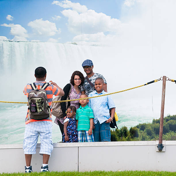 Family at Niagara Falls "Niagara Falls, Canada - May 21, 2012: Mixed race family have their photo taken in front of the Horseshoe Falls printed mural on Victoria day, National Holiday in Canada." victoria day canada photos stock pictures, royalty-free photos & images