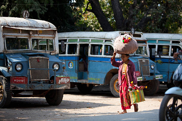 Life in Amarapura, Myanmar Amarapura, Myanmar - February 19, 2011: An old woman carrying bags full of colourful souvenirs for selling, walks along a local bus station. Amarapura, the former capital of Myanmar, means City of Immortality in Pali. It was founded after the court astrologers adviced the King to move the capital of the country to Amarapura after which the entire population of Inwa was asked to pack their belingings and migrate to the new land. Today the city is the center of weaving activities and is known to produce some of the finest festive clothing in Myanmar. Amarapura stock pictures, royalty-free photos & images