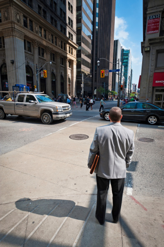 Toronto, Canada - September 13th, 2011: Man in suit stood on the sidewalk waiting to cross busy intersection between downtown skyscrapers.