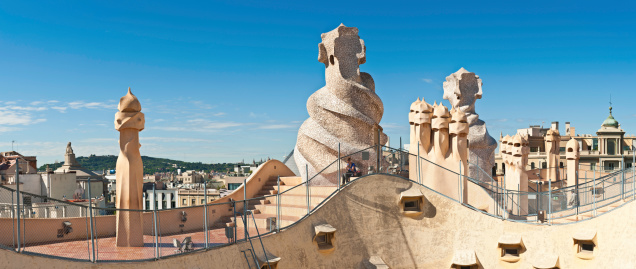 Barcelona, Spain - June 16th, 2010: Woman sitting on the steps on the rooftop of Casa Mila, La Pedrera, beside Gaudi\'s iconic chimneys and ventilation towers under blue summer skies, Barcelona, Spain. Composite panoramic image created from six contemporaneous sequential photographs.