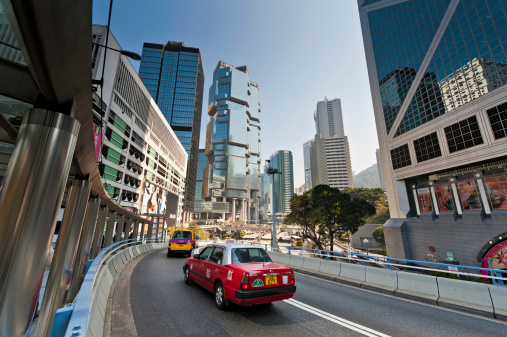Hong Kong, China - January 21st, 2011: Bright red taxi zooming through the downtown financial district of banks and skyscrapers in the crowded Central District of Hong Kong Island.