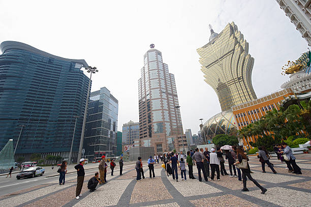 Macau, Macau S.A.R. - April 3, 2011: A group of asian tourists on Praca De Ferreira Do Amaral. The tall tower in the image center is the Bank of China office while the golden odd shape building on the right hand side is the Grand Lisboa Casino.