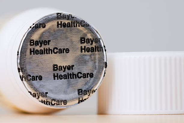 Safety Seal on Bottle of Bayer Aspirin Fosston, USA - February 25, 2011:  The unbroken foil - Bayer HealthCare - safety seal on the top of a new bottle of Bayer Aspirin next to the bottle\'s cap.  The bottle contains 24 coated tablets, 325 mg each.  Bayer HealthCare LLC. bayer schering pharma ag photos stock pictures, royalty-free photos & images