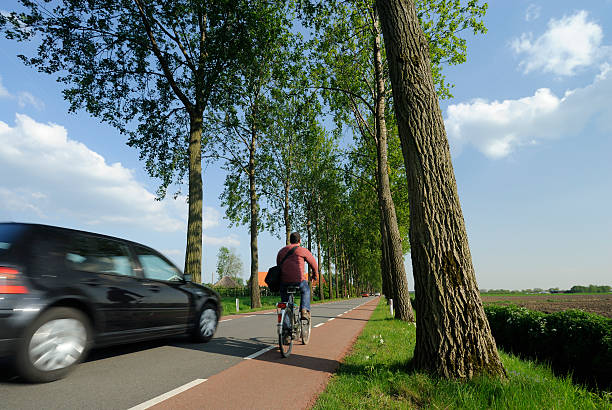 Utrecht, the Netherlands - May 6, 2008: Man cycling on a bicycle lane in a rural area a few kilometers from the city of Utrecht. A car is passing by.
